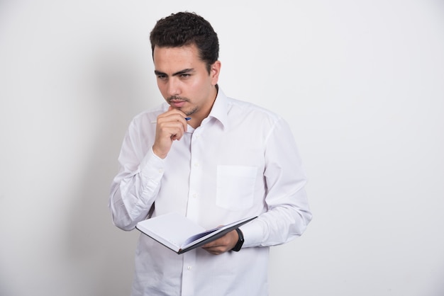 Homem de negócios sério com caderno pensando em fundo branco.