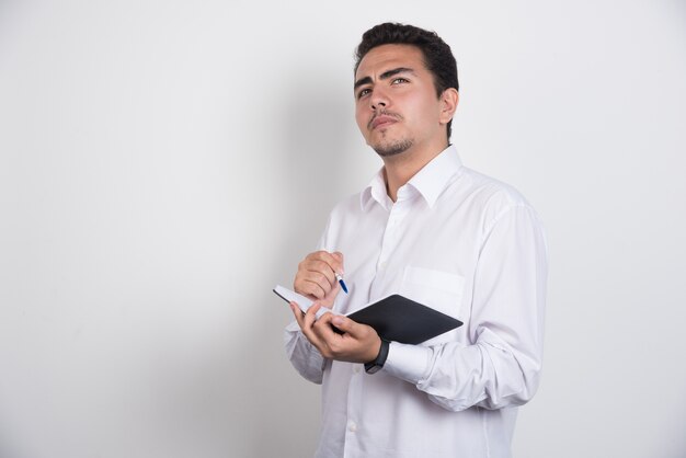 Homem de negócios sério com caneta e caderno pensando em fundo branco.