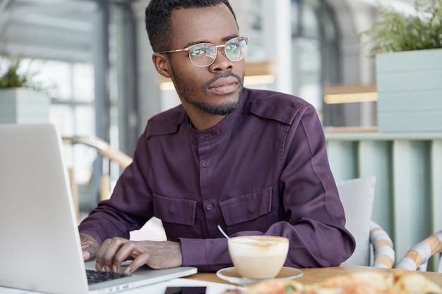 Foto grátis homem de negócios sério e pensativo de pele escura com foco em questões de trabalho, informações sobre teclados em laptop