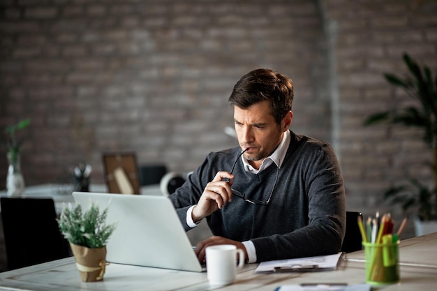 Homem de negócios sério usando laptop no trabalho e contemplando o e-mail que recebeu