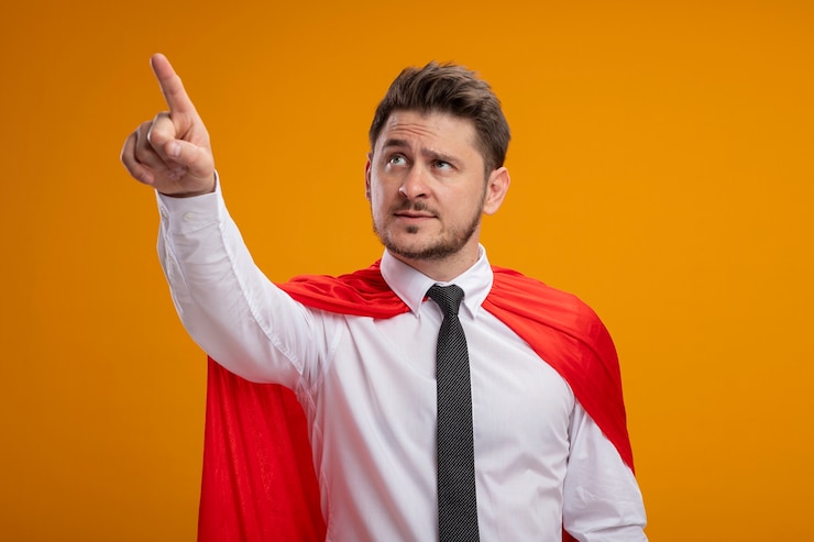 Foto grátis homem de negócios super-herói com capa vermelha olhando para algo desagradado e apontando com o dedo indicador para algo parado na parede laranja