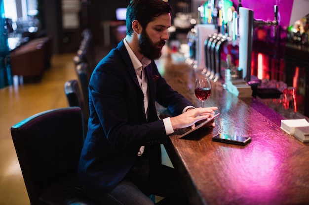 Homem de negócios usando tablet digital com copo de vinho e telefone celular no balcão