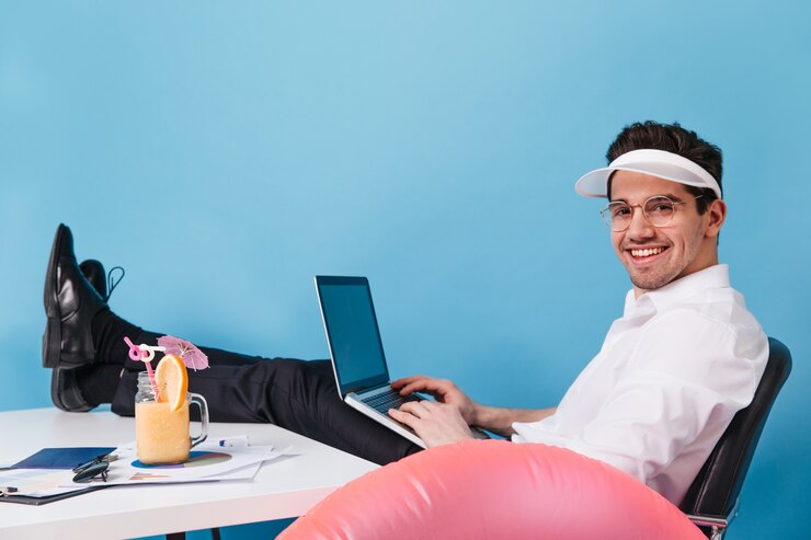Foto grátis homem de óculos e boné trabalha em um espaço isolado. cara posando com laptop, coquetel e círculo inflável.