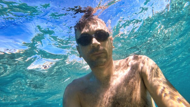 Homem de óculos, nadando sob as águas azuis e transparentes do mar Mediterrâneo. Segurando a câmera