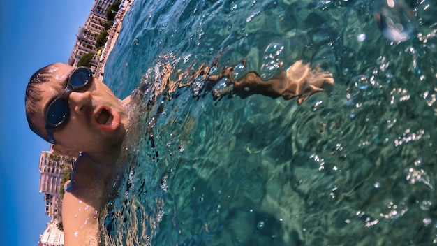 Homem de óculos, nadando sob as águas azuis e transparentes do mar Mediterrâneo. Segurando a câmera