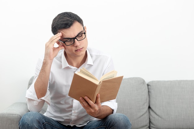 Homem de óculos, sentado no sofá e lendo o livro