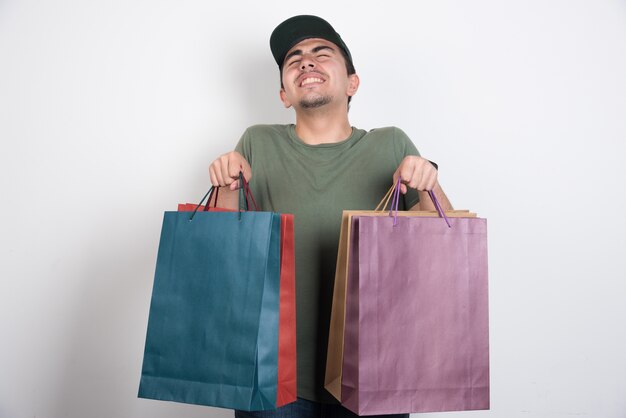 Homem de olhos fechados com sacolas de compras em fundo branco.