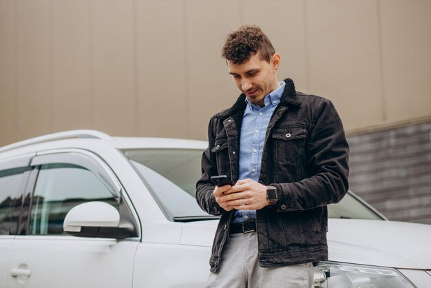 Homem de pé ao lado de seu carro e falando ao telefone