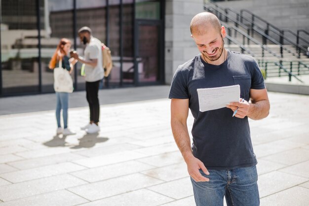 Homem de pé fora segurando bloco de notas sorrindo