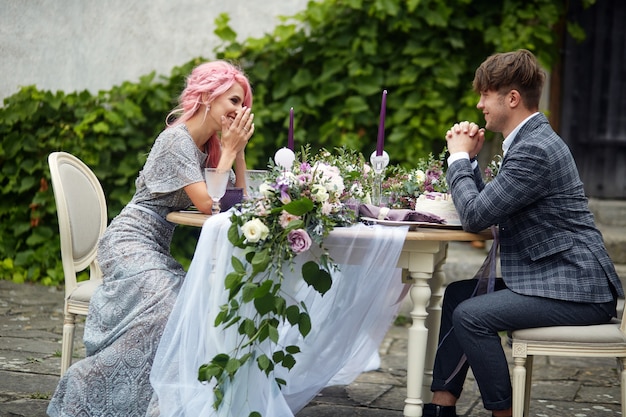 Homem de riso e sua dama de cabelo rosa sentam-se na mesa de jantar com uma decoração rosa