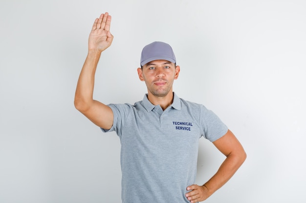 Foto grátis homem de serviço técnico segurando a palma para cima para saudação em camiseta cinza com tampa e olhando positivo