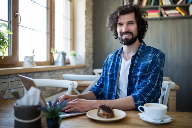 Homem de sorriso que usa o portátil na cafetaria