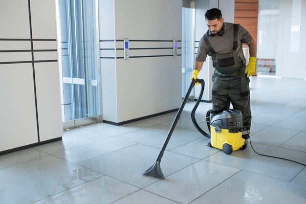 Homem de tiro completo aspirando o chão do escritório