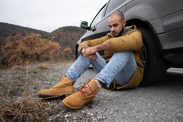 Homem de tiro completo sentado perto do carro