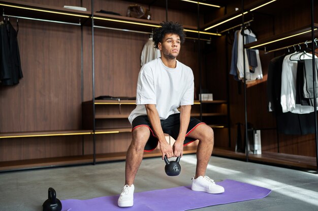 Homem de tiro completo treinando com kettlebell no tapete