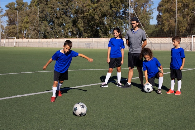 Foto grátis homem de tiro completo treinando jogadores de futebol para crianças