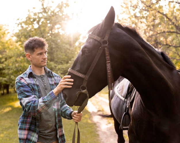 Homem de tiro médio acariciando o cavalo na natureza