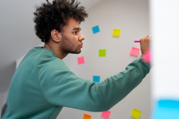 Homem de tiro médio escrevendo no post-it no trabalho