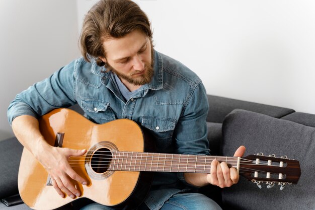 Homem de tiro médio tocando guitarra no sofá