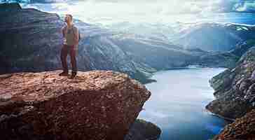 Foto grátis homem de turista de pé no trolltunga e aprecia a bela vista do fiorde norueguês.