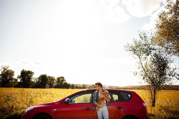 Foto grátis homem de vista frond segurando um gato na frente de um carro