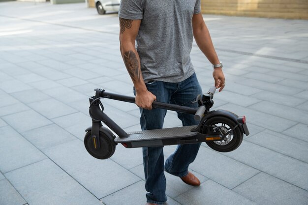 Homem de vista lateral carregando scooter elétrico
