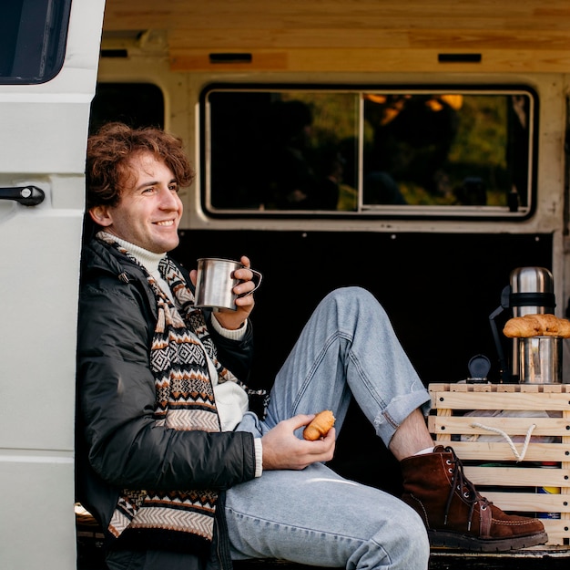Homem de vista lateral sentado em uma van bebendo café