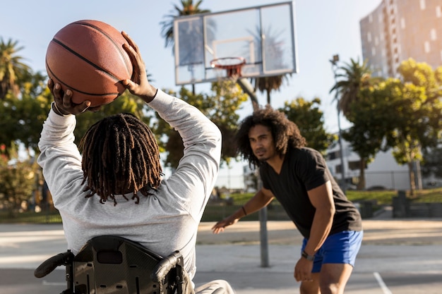 Homem deficiente em cadeira de rodas jogando basquete com os amigos ao ar livre