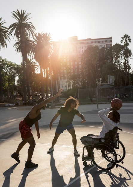 Foto grátis homem deficiente em cadeira de rodas jogando basquete com os amigos ao ar livre