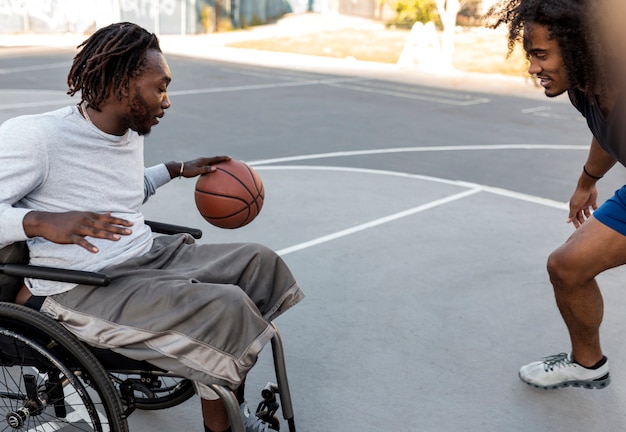 Foto grátis homem deficiente em cadeira de rodas jogando basquete com os amigos ao ar livre