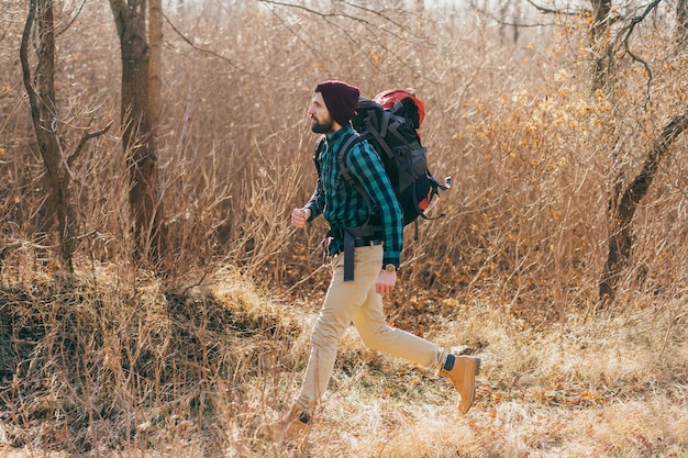 Homem descolado e moderno viajando com uma mochila na floresta de outono, vestindo uma camisa xadrez e um chapéu