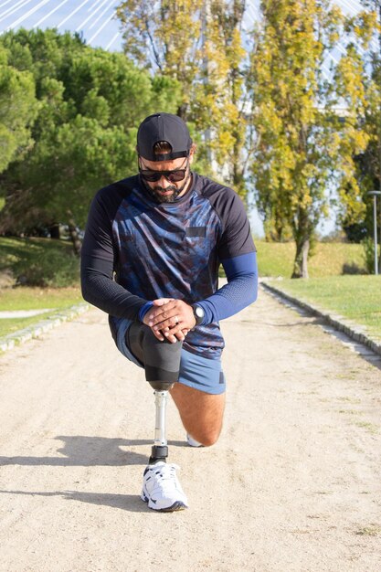 Homem desportivo com perna artificial se preparando para correr. Homem em roupas esportivas esticando as pernas no parque em dia de verão. Esporte, treinamento, conceito de bem-estar