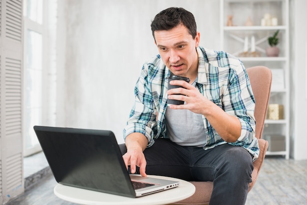 Homem, digitando, laptop, segurando, copo, bebida, cadeira