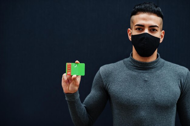 Homem do Oriente Médio de gola alta cinza e máscara de proteção de rosto preto mostra fundo isolado da bandeira do Turquemenistão