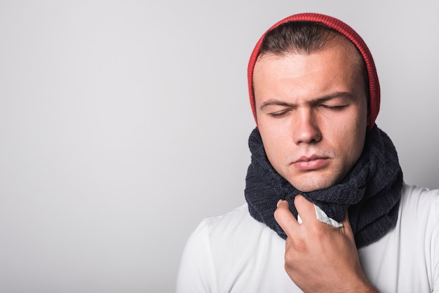 Homem doente com os olhos fechados, sofrendo de frio e tosse contra fundo branco