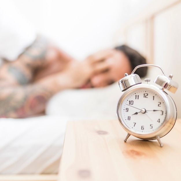 Homem dormindo com despertador na mesa de madeira