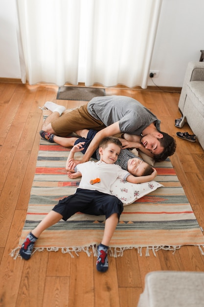 Homem dormindo com seus dois filhos no tapete em casa