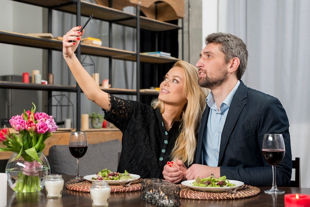 Homem e mulher alegre tomando selfie no smartphone na mesa