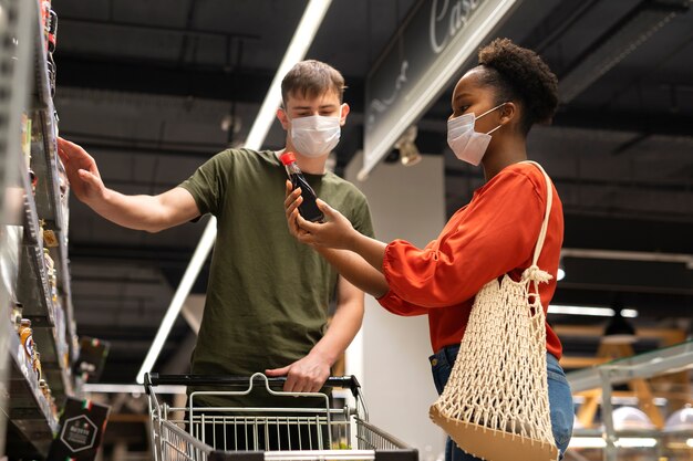 Homem e mulher com máscaras médicas fazendo compras com carrinho de compras