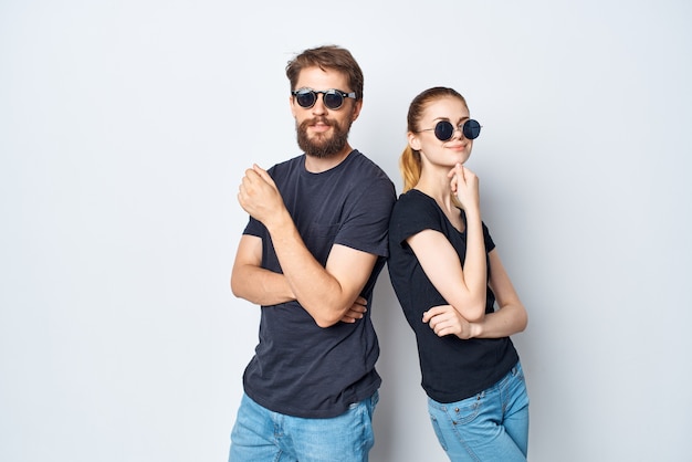 Homem e mulher elegantes em óculos de sol com camiseta preta posando com luz de fundo