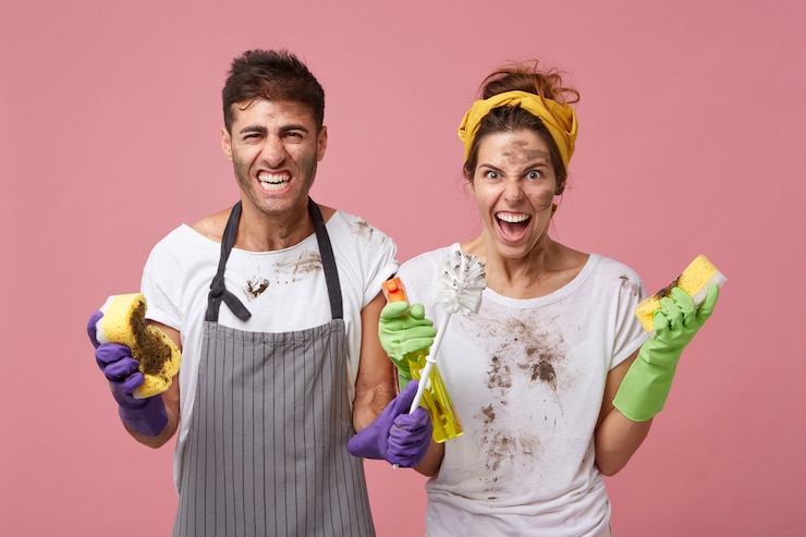 Foto grátis homem e mulher irritados do serviço de limpeza, vestindo roupas sujas, segurando o equipamento de limpeza, franzindo a testa, ocupados com a limpeza, olhando para a mobília desarrumada com nojo e raiva