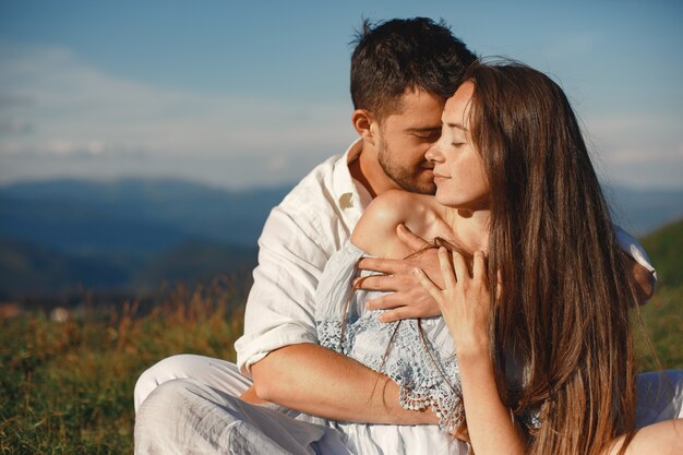 Homem e mulher nas montanhas. Jovem casal apaixonado ao pôr do sol. Mulher de vestido azul.