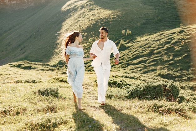 Homem e mulher nas montanhas. jovem casal apaixonado ao pôr do sol. mulher de vestido azul.