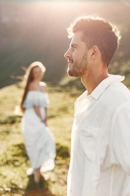 Homem e mulher nas montanhas. Jovem casal apaixonado ao pôr do sol. Mulher de vestido azul.