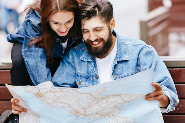 Homem e mulher olham o mapa sentado no banco em algum lugar de uma cidade velha