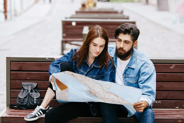 Homem e mulher olham o mapa sentado no banco em algum lugar de uma cidade velha