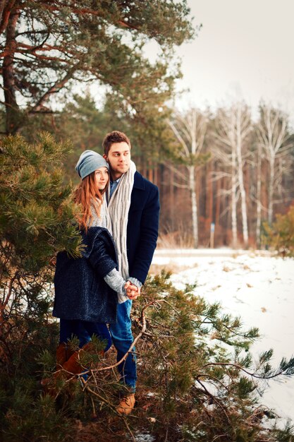 Homem e mulher posando ao lado de um pinheiro em um dia de inverno