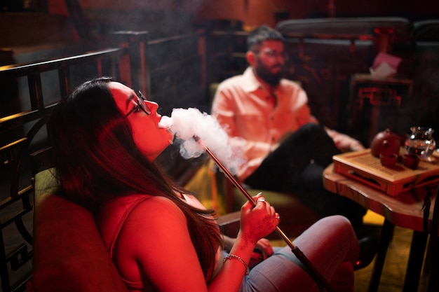 Foto grátis homem e mulher relaxando fumando um narguilé em um bar