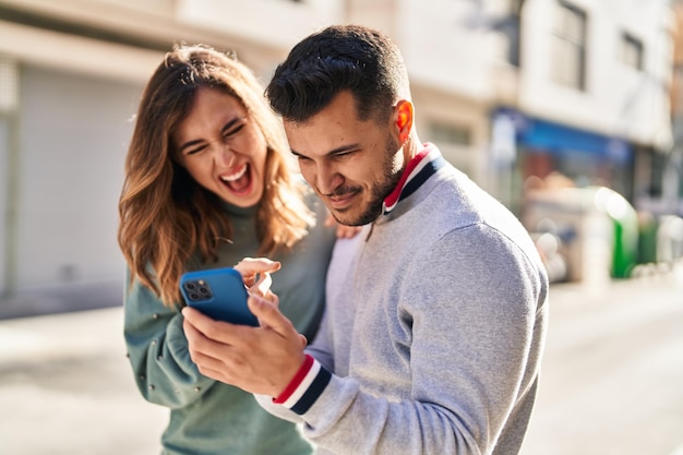 Foto grátis homem e mulher sorrindo confiantes usando smartphone na rua