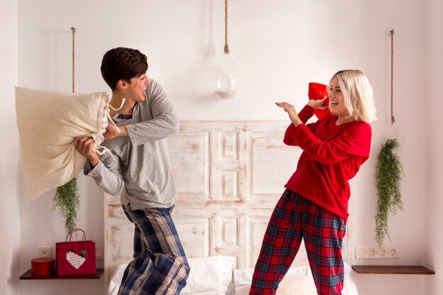 Homem e mulher tendo uma luta de almofadas no quarto